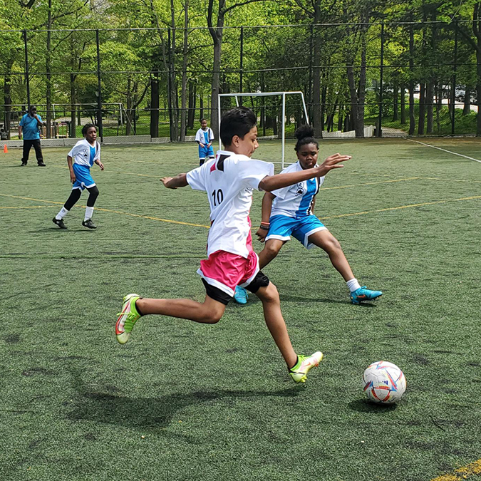 kids from an NYC Parks rec center program run for a soccer ball in their custom team uniforms